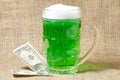 Glass of Irish green beer and dollars on a burlap background