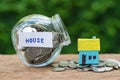 glass jar bottle labeled as house with full of coins and miniature house on stack of coins as home, property or mortgage