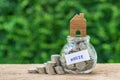 glass jar bottle labeled as house with full of coins and miniature wooden house on top and stack of coins as home, property or mo