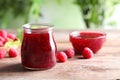 Glass jar and bowl of sweet jam with ripe raspberries on wooden table against blurred background. Royalty Free Stock Photo