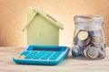 Glass jar with coins, calculator and home replica on wooden desk for home loans