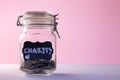Glass jar with coins with chalk tag Charity on a pink background. Donation and charity concept. Copy space. Royalty Free Stock Photo