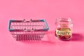 Glass jar with coins and inscription equity near empty market basket lies on pink Royalty Free Stock Photo