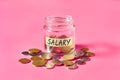 Glass jar with coins and inscription salary lies on pink