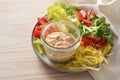 Glass jar with creamy dressing of skyr on a plate with raw salad like lettuce, chicory and tomatoes, light wooden table with copy
