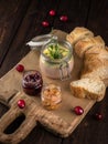 Glass jar of duck liver pate with cranberries and slices of bread on the wooden chopping board. Dark brown texture background. Royalty Free Stock Photo