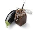 Glass jar with eggplant chutney and a fresh eggplant on the side on white background