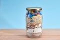 Glass jar filled with cookie mix, which includes colorful candies, cereal, flour, brown, white sugar and chocolate powder, covered