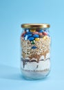 Glass jar filled with cookie mix, which includes layers of colorful candies, cereal, flour, brown and white sugar and chocolate