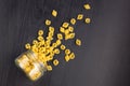 Glass jar filled with dry farfalle pasta and scattered around on black background