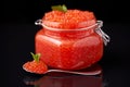 A glass jar filled with red caviar with a spoon with red caviar next to a dark, reflective background. Caviar, Russian food Royalty Free Stock Photo