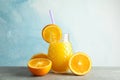 Glass jar with fresh orange juice, tubule and oranges on grey table against color background, space for text