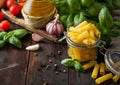 Glass jar of fresh raw penne pasta with oil and garlic, basil plant and tomatoes on wooden background Royalty Free Stock Photo