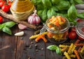 Glass jar of fresh raw tricolor fusilli pasta with oil and garlic  basil plant and tomatoes on wooden background Royalty Free Stock Photo