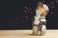 Glass jar with full of coins and light bulb on top on wooden table to show concept saving money, hope, future, education, home Royalty Free Stock Photo