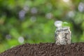 A glass jar with full coins and plant growing on top with soil to show concept saving money Royalty Free Stock Photo