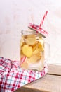 Glass jar with ginger water with straw and red tartan cap on red checkered cloth on wooden planks on light background. Royalty Free Stock Photo