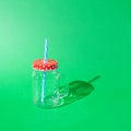 Glass jar with handle, empty, red lid with white dots, white straw with blue stripes. Harsh shadow. Green background. Text space. Royalty Free Stock Photo