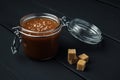 A glass jar with homemade salted caramel and a few pieces of brown sugar Royalty Free Stock Photo