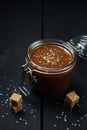 A glass jar with homemade salted caramel and a few pieces of brown sugar with salt crystals Royalty Free Stock Photo