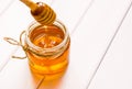 Glass jar with honey and dipper on white wooden table background