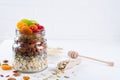 Glass jar with ingredients for cooking granola on white background. Oat flakes, honey, nuts, dried fruit and seeds.