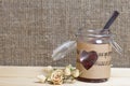 Glass jar of jam wrapped in paper with notes. Heart cut out in paper. Nearby dried roses. It stands on the boards, on the Royalty Free Stock Photo