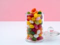 glass jar with lid filled with colorful candies on bright pink background