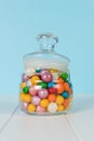 A glass jar with a lid filled with colorful candies on a wooden table