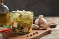 Glass jar of marinated feta cheese on wooden table