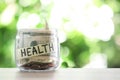 Glass jar with money and label HEALTH on table against blurred background.