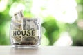 Glass jar with money and label HOUSE on table against blurred background