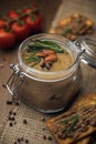 Glass jar with poultry pate, decorated with almonds and rosemary, crackers with pate and red cocktail tomatoes on the sackcloth