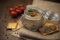 Glass jar with poultry pate, decorated with almonds and rosemary, crackers with pate and red cocktail tomatoes on the sackcloth