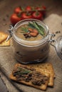 Glass jar with poultry pate, decorated with almonds and rosemary, crackers with pate and red cocktail tomatoes on the sackcloth