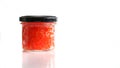 Glass jar with red salmon caviar, closed with a black metal lid. White background. Copy space for an inscription Royalty Free Stock Photo