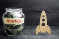 Glass jar, rocket and the word `Startup`. The concept of raising funds for a startup. Charitable contributions to translate ideas Royalty Free Stock Photo