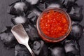 Glass jar with salmon caviar standing in the middle of ice cubes on black slate plate Royalty Free Stock Photo