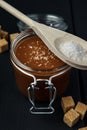 Glass jar of salted caramel with a wooden spoon of salt and a few slices of brown cane sugar Royalty Free Stock Photo