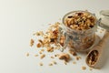 Glass jar and scoop with granola on white background