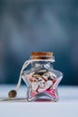 A glass jar in the shape of a star inside pink sand and small shells on a blue background close-up.Maritime concept Royalty Free Stock Photo
