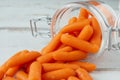 Glass jar with small peeled pieces of baby carrot on white wooden table