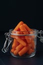 Glass jar with small peeled pieces of carrot on dark textured background