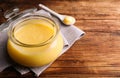 Glass jar and spoon of Ghee butter on wooden table, closeup. Space for text