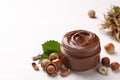 Glass jar with tasty chocolate spread, hazelnuts and green leaves on light background Royalty Free Stock Photo