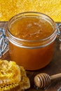 A glass jar of thick golden honey with a wooden spoon and honeycombs. Concept of beekeeping, apiculture, apiary. Sweet honey