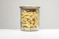 Glass jar with a wooden lid filled with dried pasta for cooking on a white surface and white background Royalty Free Stock Photo