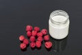 Glass jar with yogurt and seven raspberries on a black background.