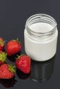 Glass jar with yogurt and six strawberries on a black background. Royalty Free Stock Photo