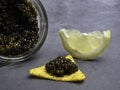 Glass jars with black caviar, lemon on grey background